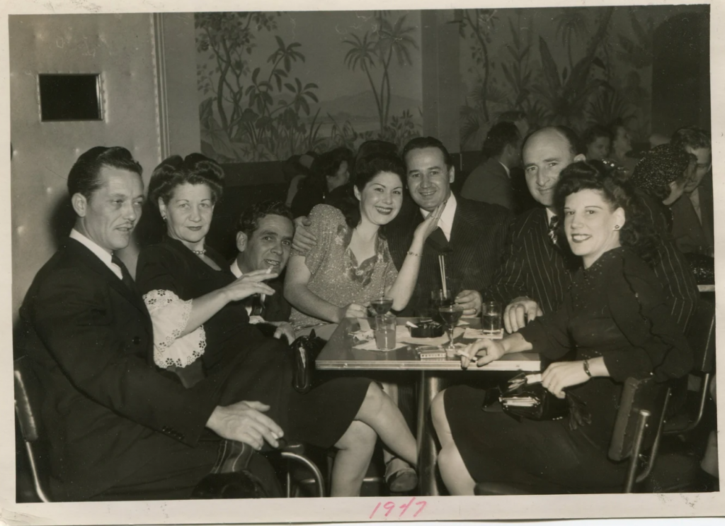 1940s vintage photo from 1947 of a group of people in a bar enjoying themselves with friends. The women are wearing 1940s dresses and 1940s hairstyles