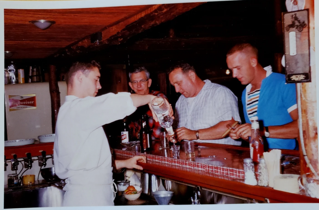 1960s vintage photo of a bartender serving people at the bar in the 1960s. One man is holding a cigar. 