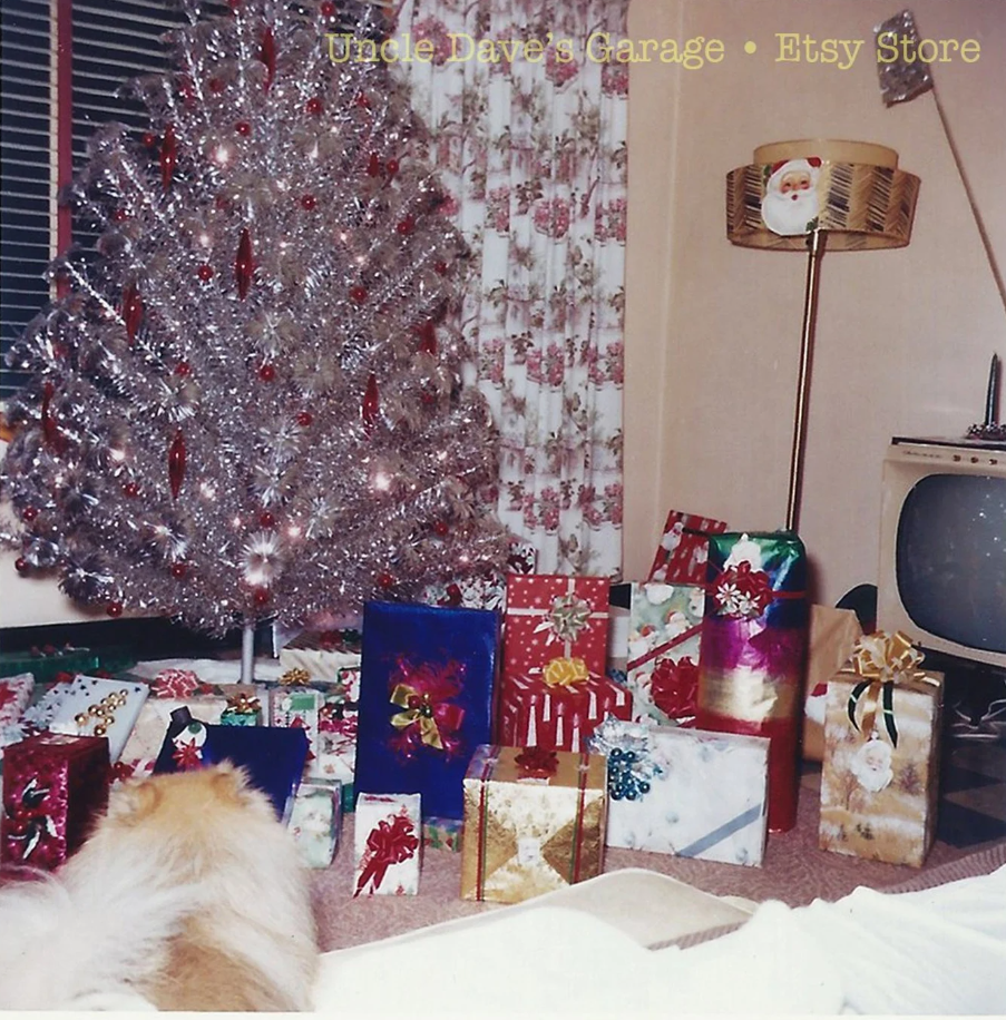 1960s vintage photo of a mid century home with an aluminum christmas tree surrounded by gifts and mid century tv and fiberglass lamp