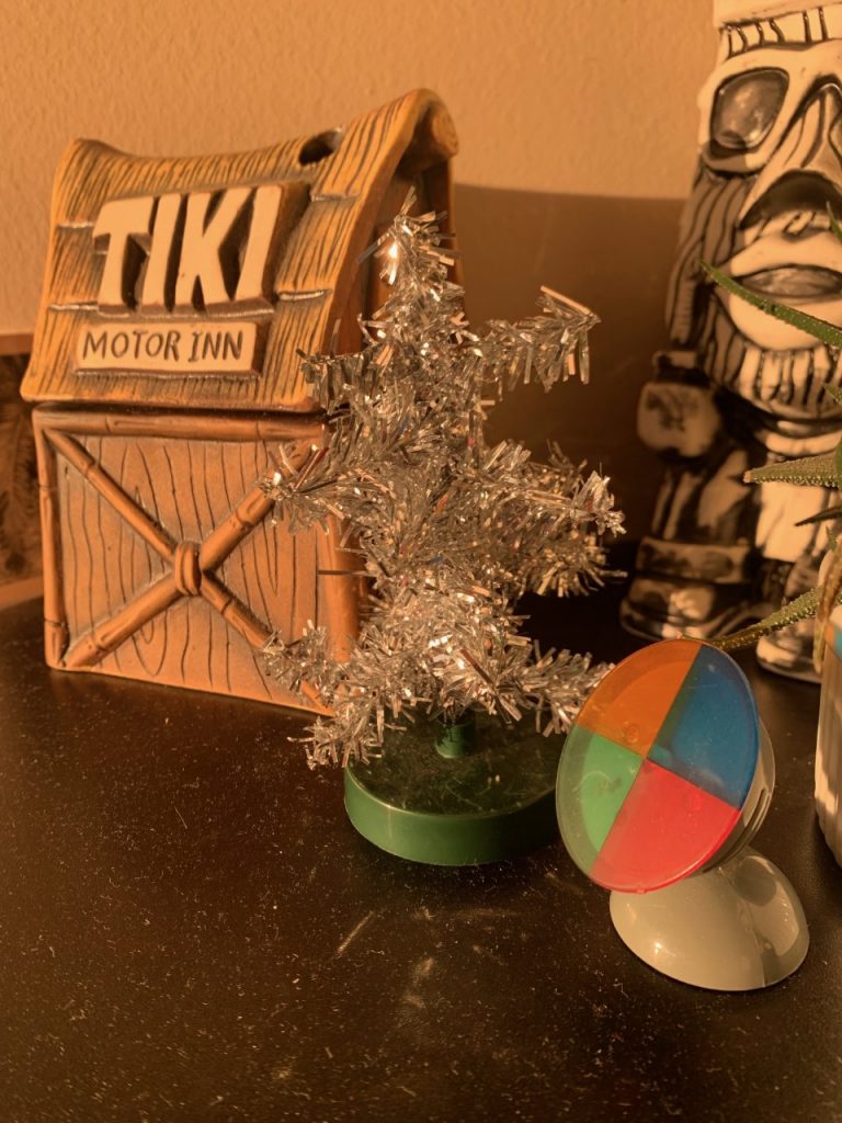 tiny aluminum christmas tree with color wheel beside a tiki motor inn tiki mug