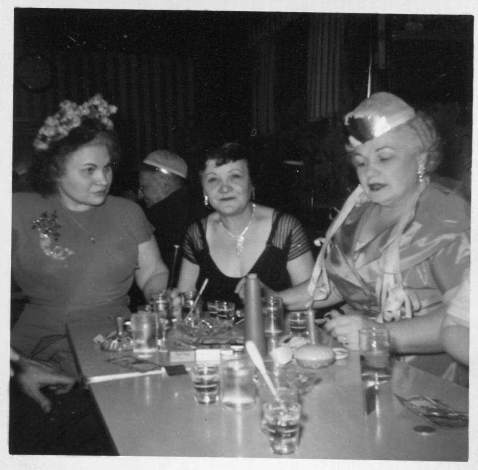 1950s vintage photo of 3 older women in celebrating New Year's Eve at a bar in 1950s fashions. 