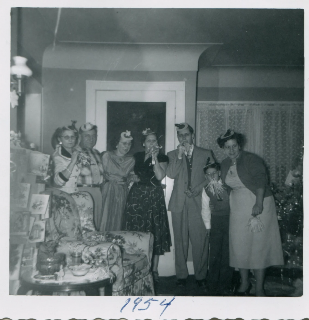 1950s vintage photo of a New Years eve house party. Photo is a group with party hats and 1950s fashions posing together blowing noise makers