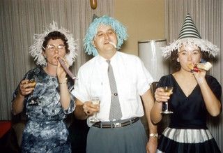 1960s vintage photo of a 1960s New Years Eve party feaaturing three people in 1960s clothing with party hats and horn blowers. 