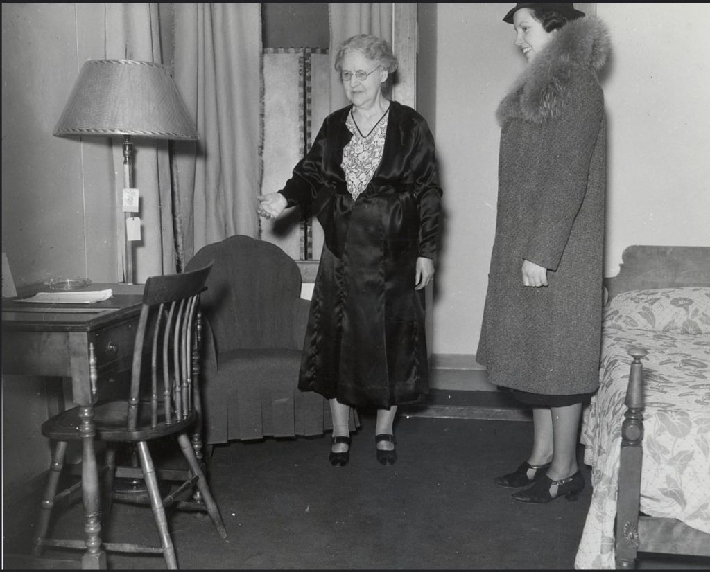 1930s vintage photo of two women one older and one younger in 1930s fashions looking at what a dorm room looks like at the University of Wisconsin Madison