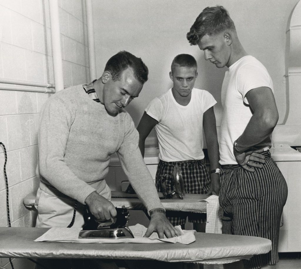 1950s vintage photo of two young men in university learning how to iron while staying in the dorms. Dorm Life