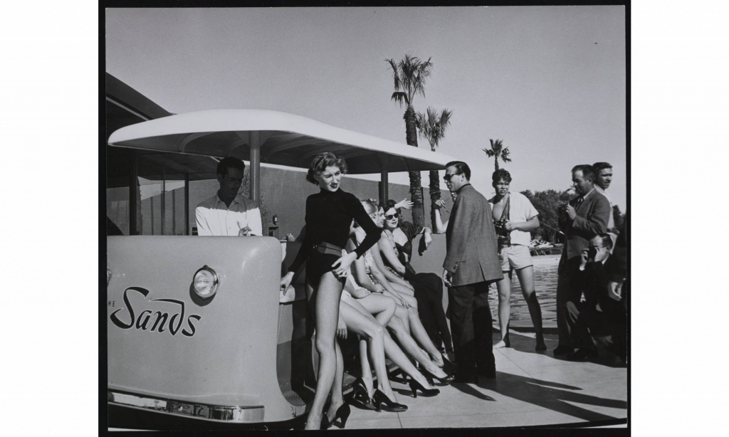 1960s vintage photo ofa group of men and women in 1960s fashions hanging out at the Sands Hotel pool.