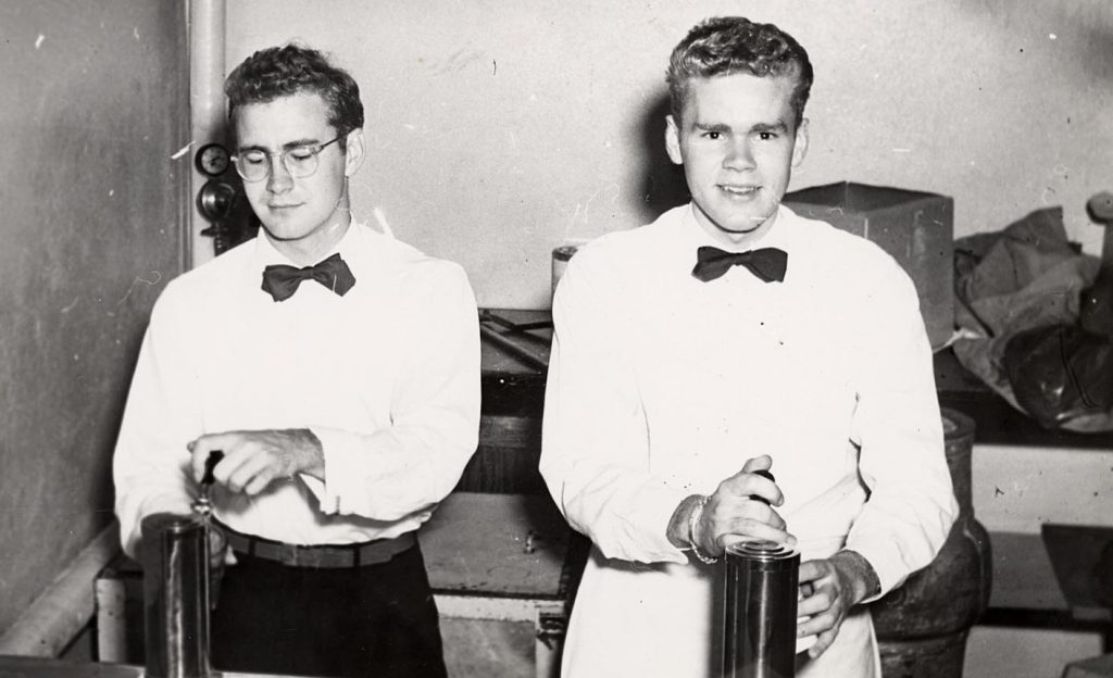 1940s vintage photo from the University of Wisconsin-Madison of 2 young men,  Jack Vazina and Dave Thompson, in waiter uniforms, work the bar during a party in Swenson house of Kronshage hall. C. 1949. Vintage Dorm Life. 