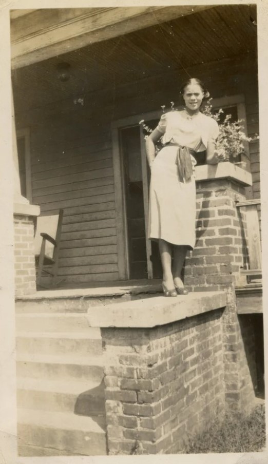 1930s vintage photo of a young woman in 1930s dress posing on the step ledge of her home