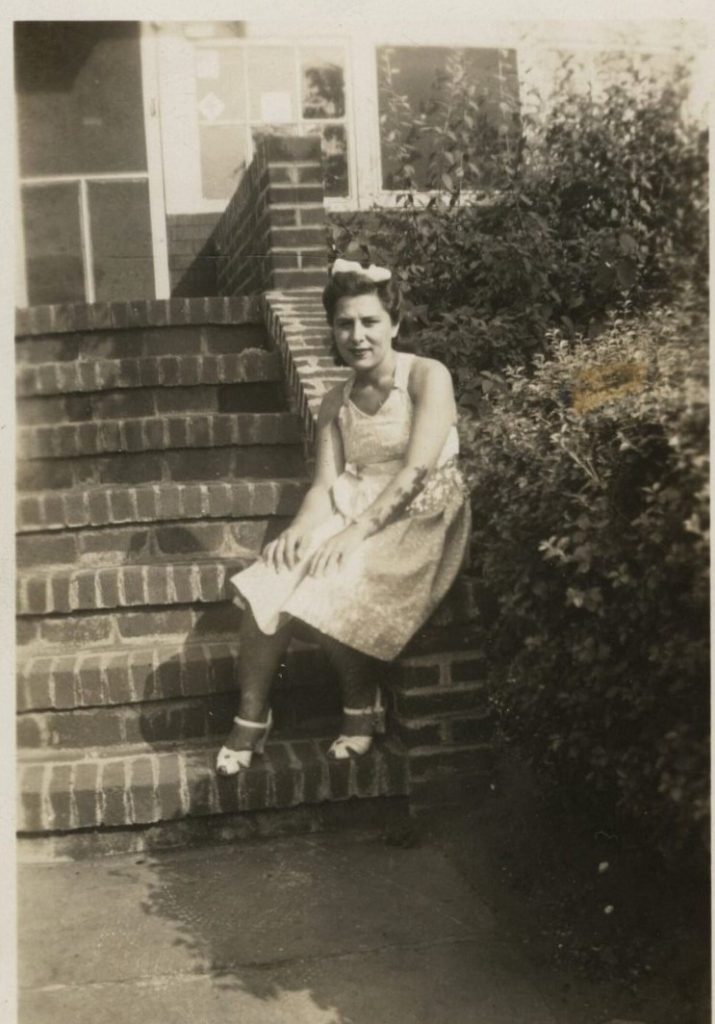 1940s vintage photo of a woman in a 1940s summer dress, white peep toe shoes and a bow in her 1940s hairstyle posing on the steps of her home. Super 1940s Fashion Inspiration