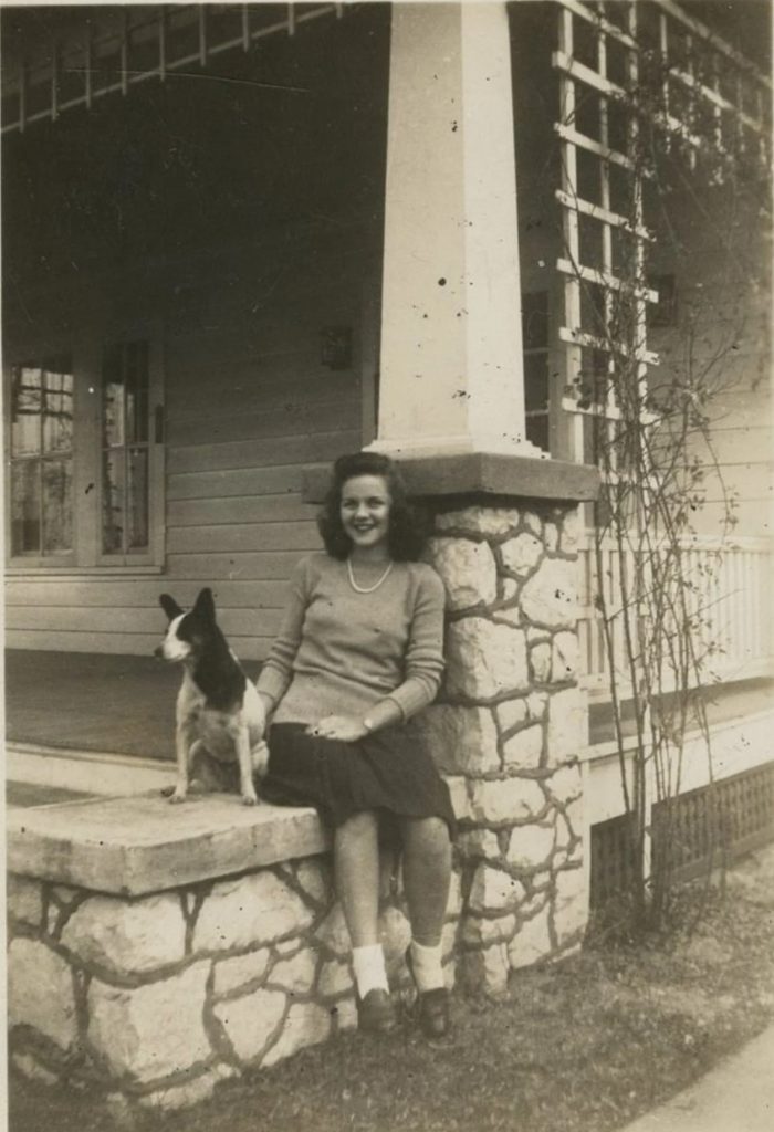 1940s vintage photo of a young woman posing with her dog at the front of her house in 1940s hairstyle and 1940s fashion