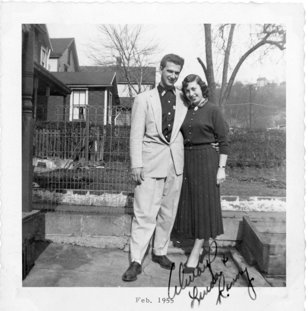 1950s vintage photo of a stylish 1950s couple in 1950s fashions posing for a photo together. Woman is wearing a knitted skirt & knitted matching cardigan. February 1955