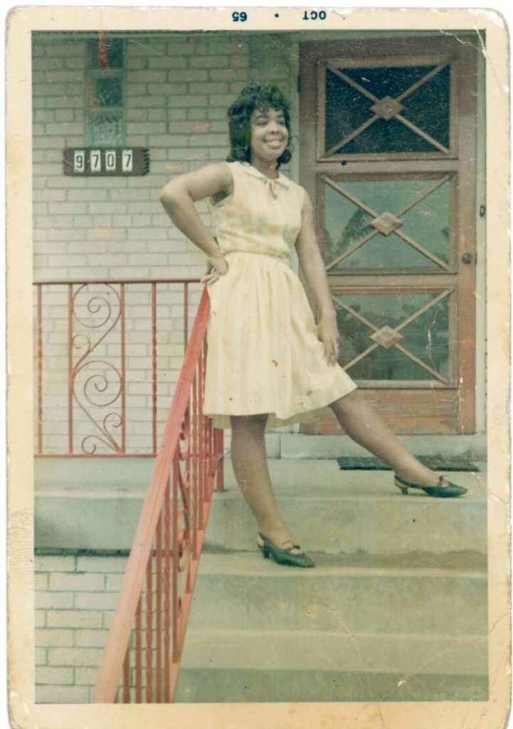 1960s vintage photo of a young Black Woman in a 1960s dress and 1960s shoes posing on the steps of her house