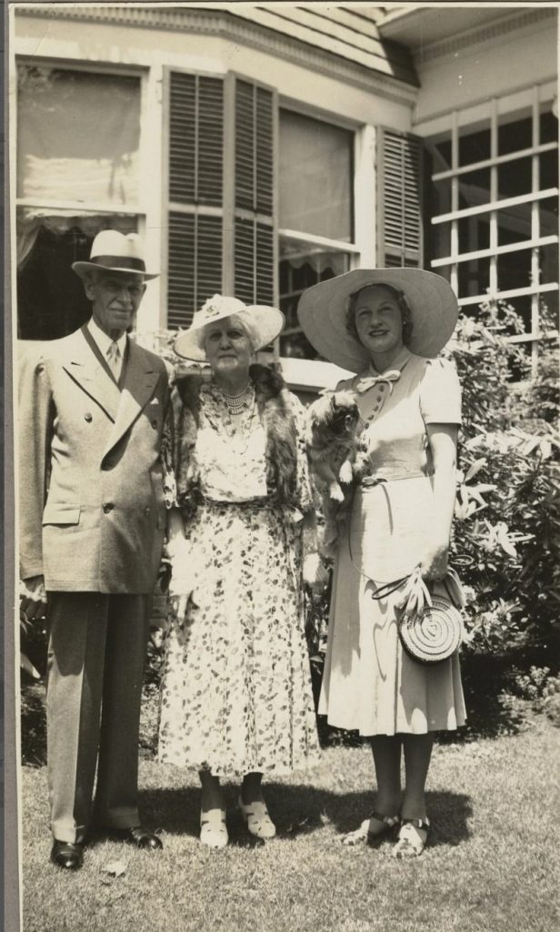 Late 1930s vintage photo of an older couple posing with a young woman holding a dog. They are all dressed up in hats and lovely 1930s dresses (and one suit). I especially love our young woman's dress & that awesome circle rattan purse.