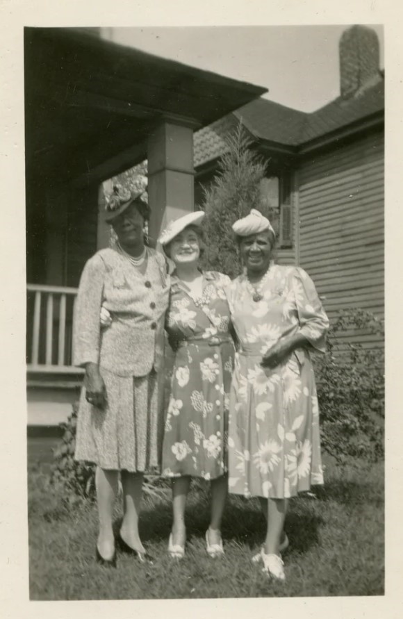 Late 1940s photo of three women all dressed up in floral dresses and one two piece suit with 1940s hats including one turban hat. 