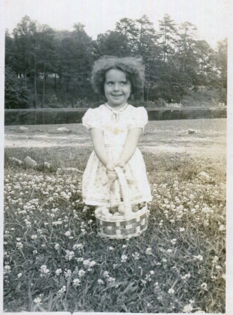 1930s vintage photo of a cute girl holding an easter basket in a field of flowers