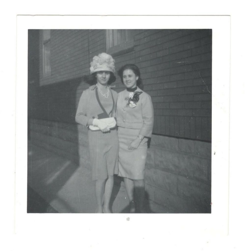 1960s vintage photo of two stylish young women in 1960s fashions one woman is wearing a large 1960s hat both are wearing corsages on their dresses