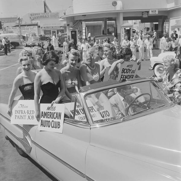 1950s vintage photo from 1951 of a beauty pageant contestants of a dealership representing various departments of the shop. In this photo they are all posing in a car in 1950s swimsuits. 