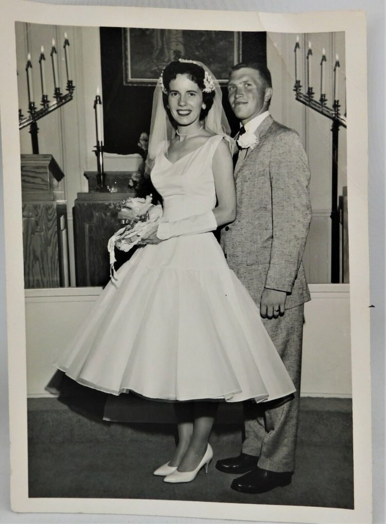 1950s vintage wedding photo of a 1950s bride in a tea length 1950s wedding dress posing with her crew cut groom