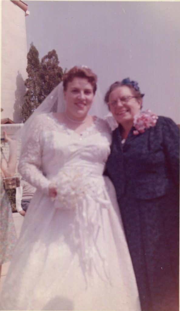 1950s vintage wedding photo of a pretty plus sized 1950s bride in her wedding dress posing with her happy mother