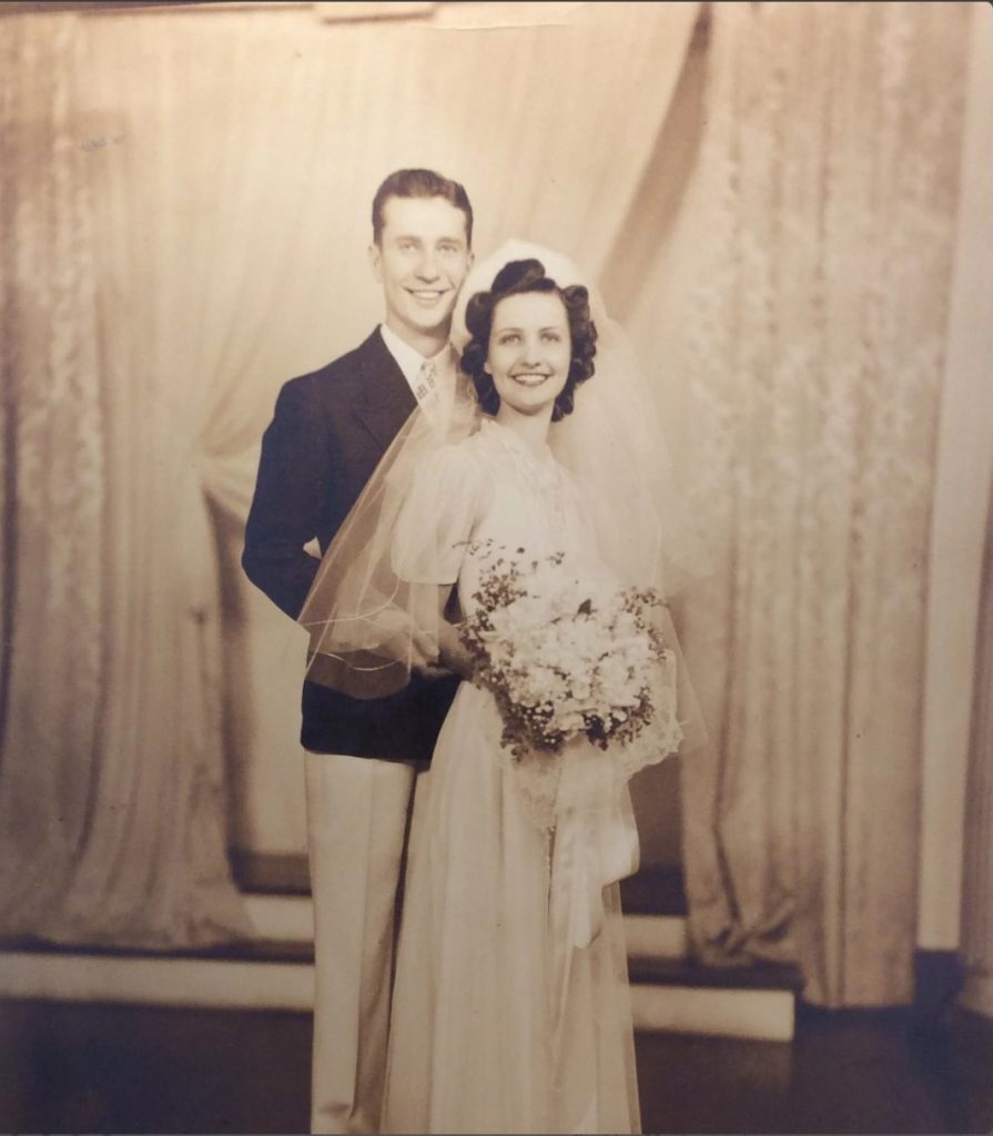 late 1930s early 1940s vintage wedding photo of a young bride and groom posing for their photo. The woman has a beautiful curled hair vintage hairstyle