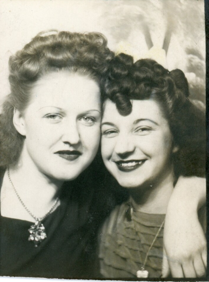 1940s vintage photo of two young women posing together in a photobooth with beautiful 1940s hairstyles, heads full of curls. 