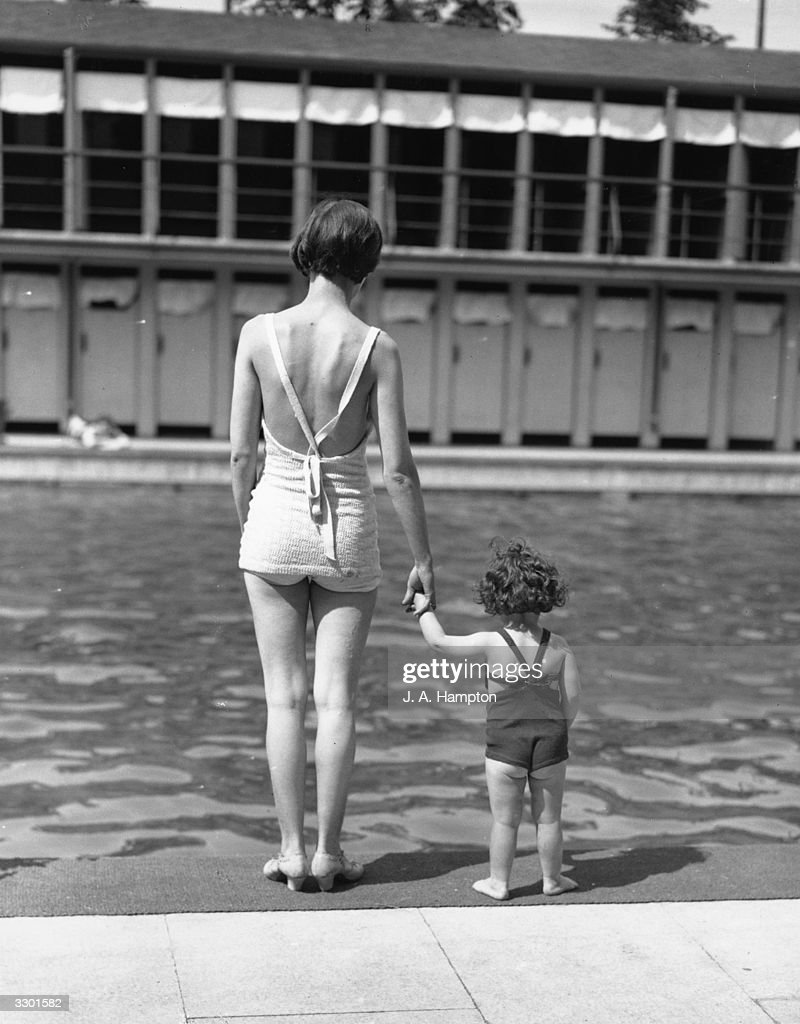 1930s vintage photo: 27th May 1934:  A mother and daughter standing hand in hand at the edge of Chiswick Open Air Swimming Pool, west London.  (Photo by J. A. Hampton/Topical Press Agency/Getty Images)