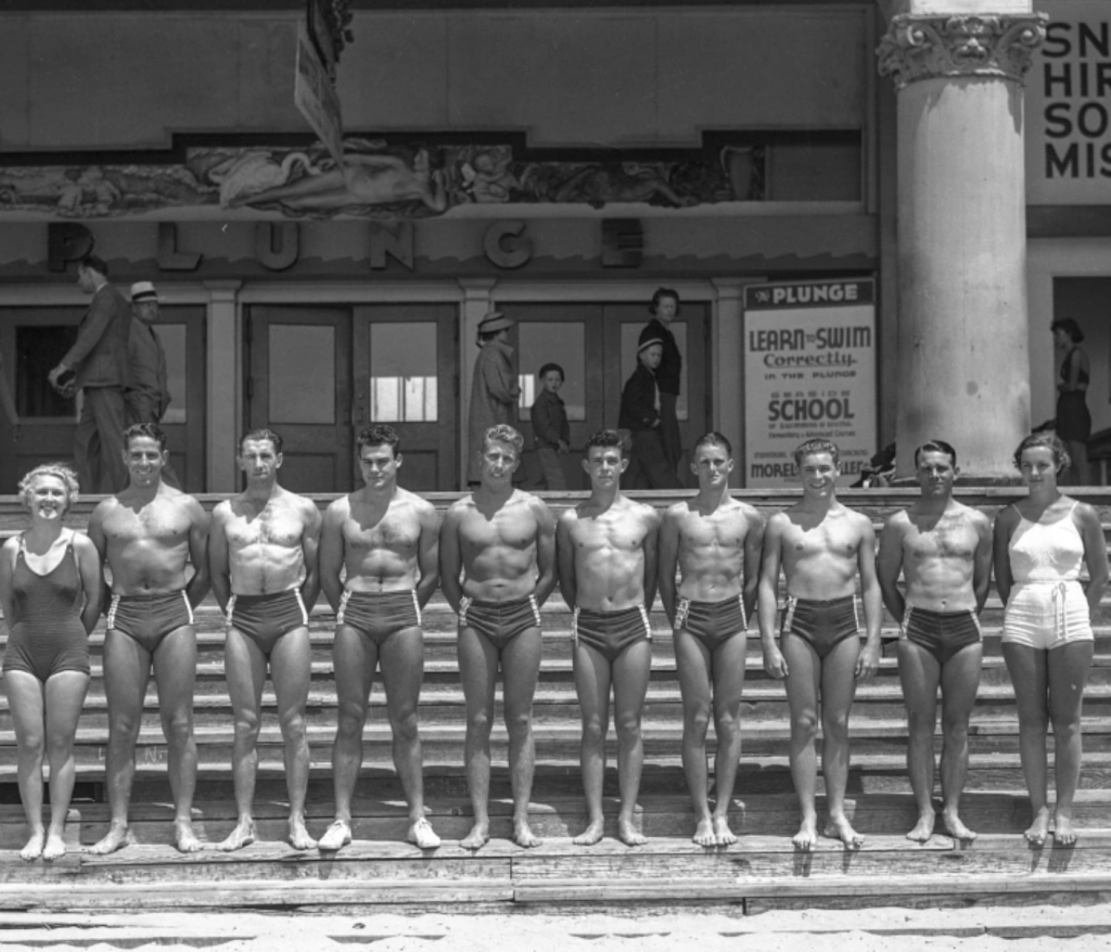 1930s vintage photo. These young men and women pose on the steps to the Santa Cruz Boardwalk’s giant indoor saltwater swimming pool, called The Plunge.

Although this late 1930s photograph was uncaptioned, this group was most likely promoting one of the Boardwalk’s famous water shows. The man at the far left is Don Patterson, who was famous for many death-defying stunts designed to draw tourists to the Boardwalk.

His most famous act involved donning an asbestos suit, lighting himself on fire, and diving into the pool.