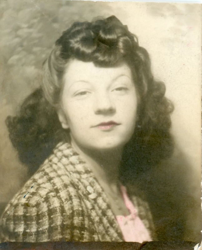 1940s vintage photo (tinted) of a young women in a photo booth with a 1940s hairstyle of curls. Super 1940s vintage hairstyle inspiration.