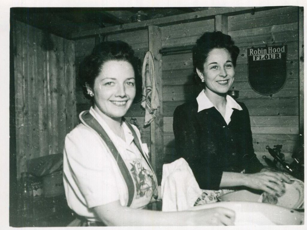 1940s vintage photo of two women in a cottage washing dishes with a robin hood flour sign in the background on the wall.