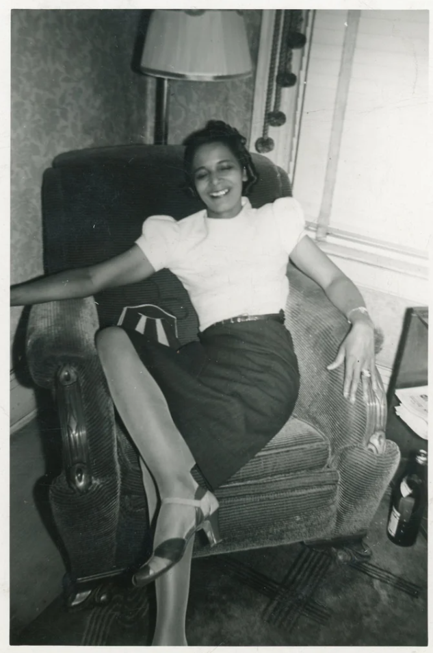 1950s vintage photo of a Black Women in a pencil skirt and white top a cool 1950s shoes chilling in a chair in the living room