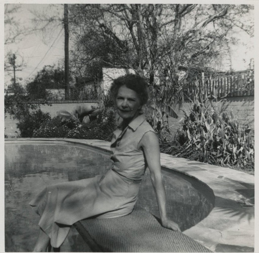 1950s vintage photo of an older woman in a 1950s skirt and top sitting on a diving board at her pool in her backyard