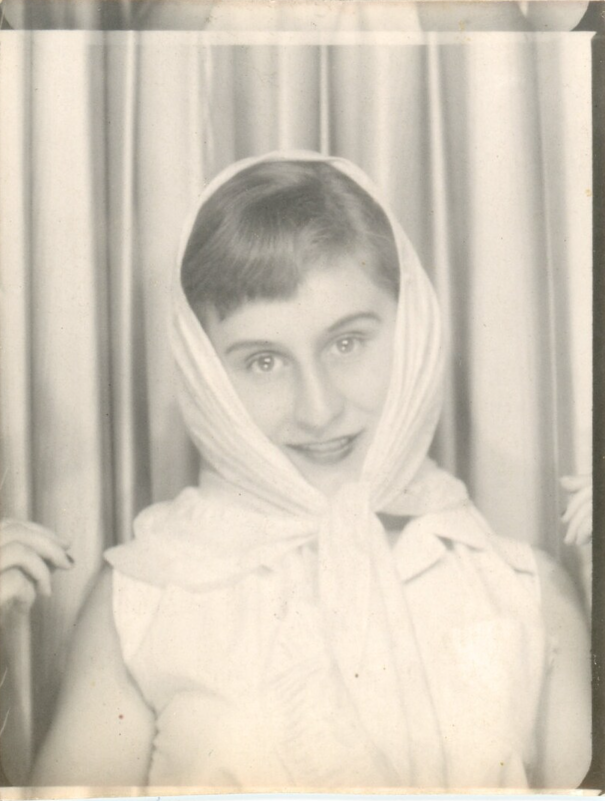 1950s vintage photo booth image of a young girl wearing a scarf on her head tied at the neck and posing for a photo