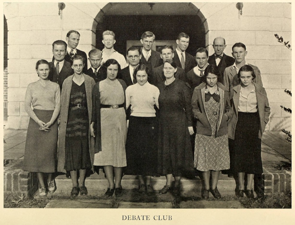 1930s Vintage Yearbook photo from 1934 of the Debate Team from   The image features young men and women in 1930s fashions posing together on the steps of the school. 