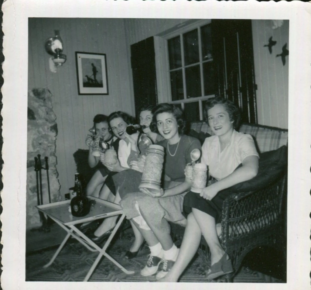 1940s vintage photo of young women in 1940s fashions including saddles shoes holding beers and beer steins at a party