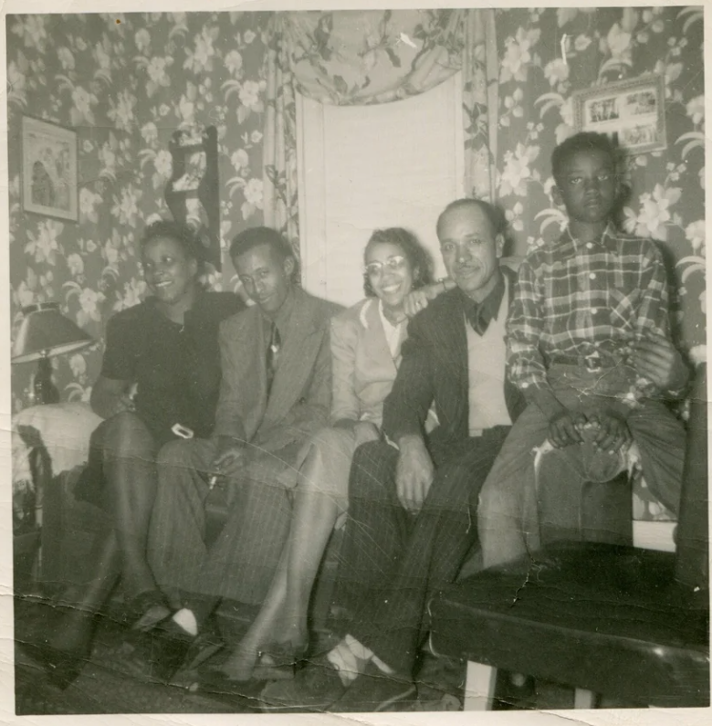 1950s vintage photo of a Black-family posing on a couch together for a photo in their living room with the floral wallpaper. Fun Mid Century Interior Design.