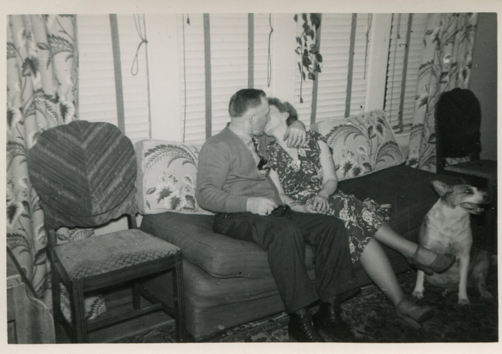 1940s / 1950s vintage photo of a couple kissing on their couch in their living room while their dog is nearby