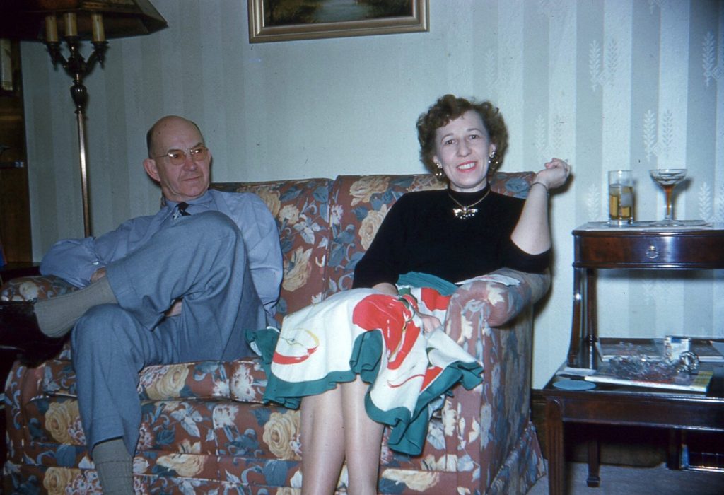 1950s vintage photo of a Couple Having Cocktails on their living room couch. The woman is wearing a 1950s novelty skirt of fruit. 