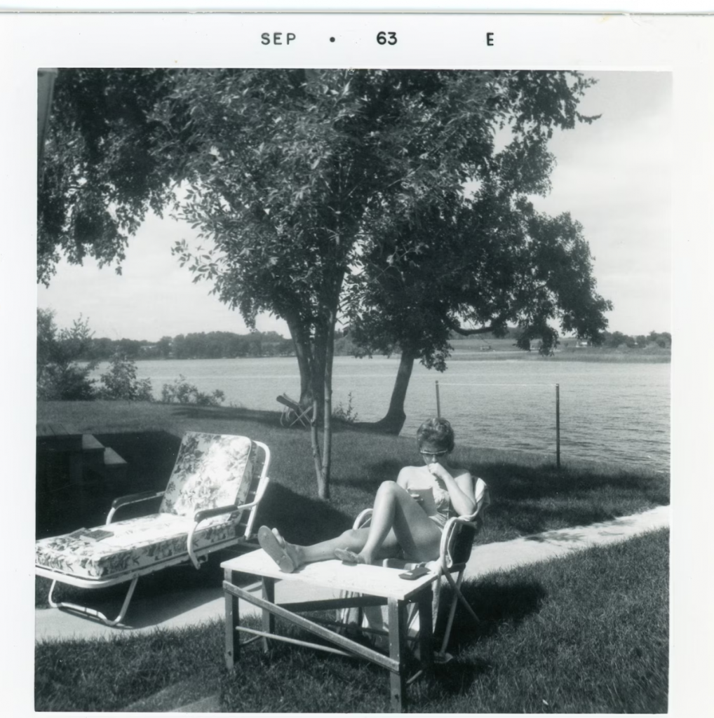 1960s vintage photo: Woman in Bathing Suit Reading in Sun Lounge Chair by the lake. 