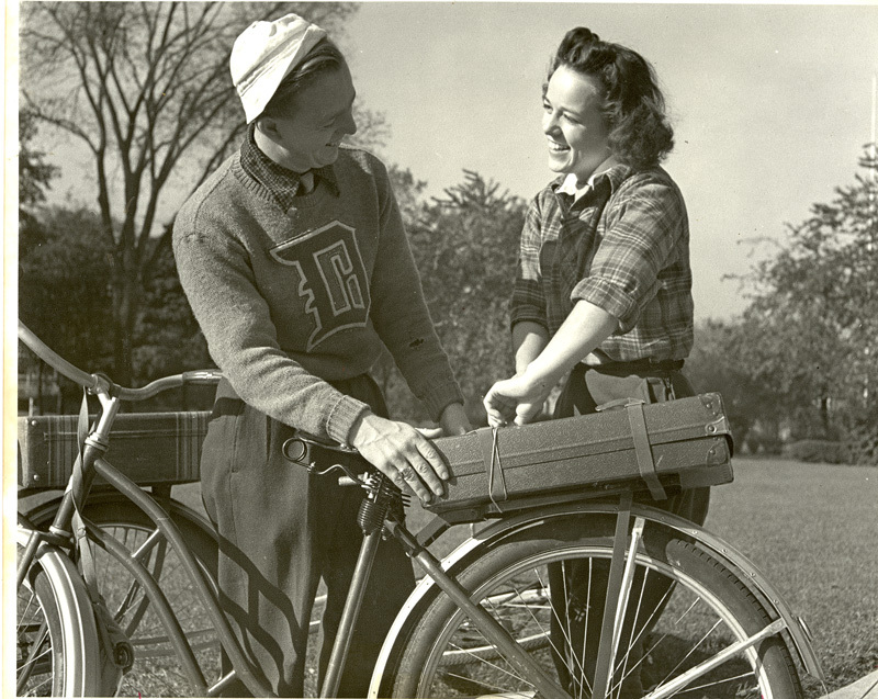 1940s photo. Western Connecticut State University students share a chat beside a bicycle. The young man is proudly sporting his letterman sweater. 