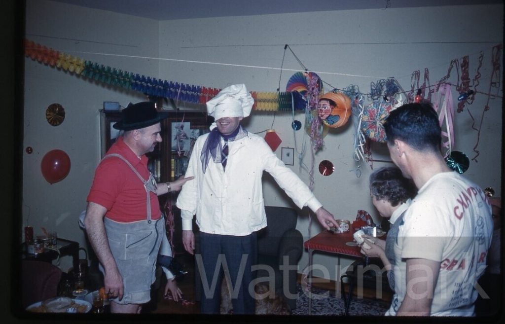 1950s vintage photo of a Halloween Party featuring guests in Halloween Costumes like a chef and a man in lederhosen. 