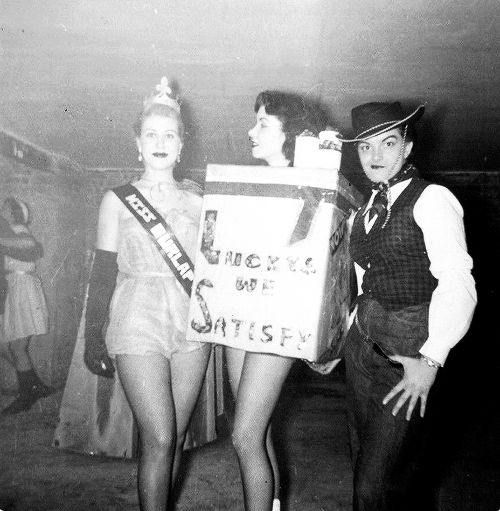 1950s vintage photo of a halloween party featuring a woman dressed as lucky strike cigarettes a woman as a cowgirl and another woman as a beauty pageant contestant..Miss Burlap.