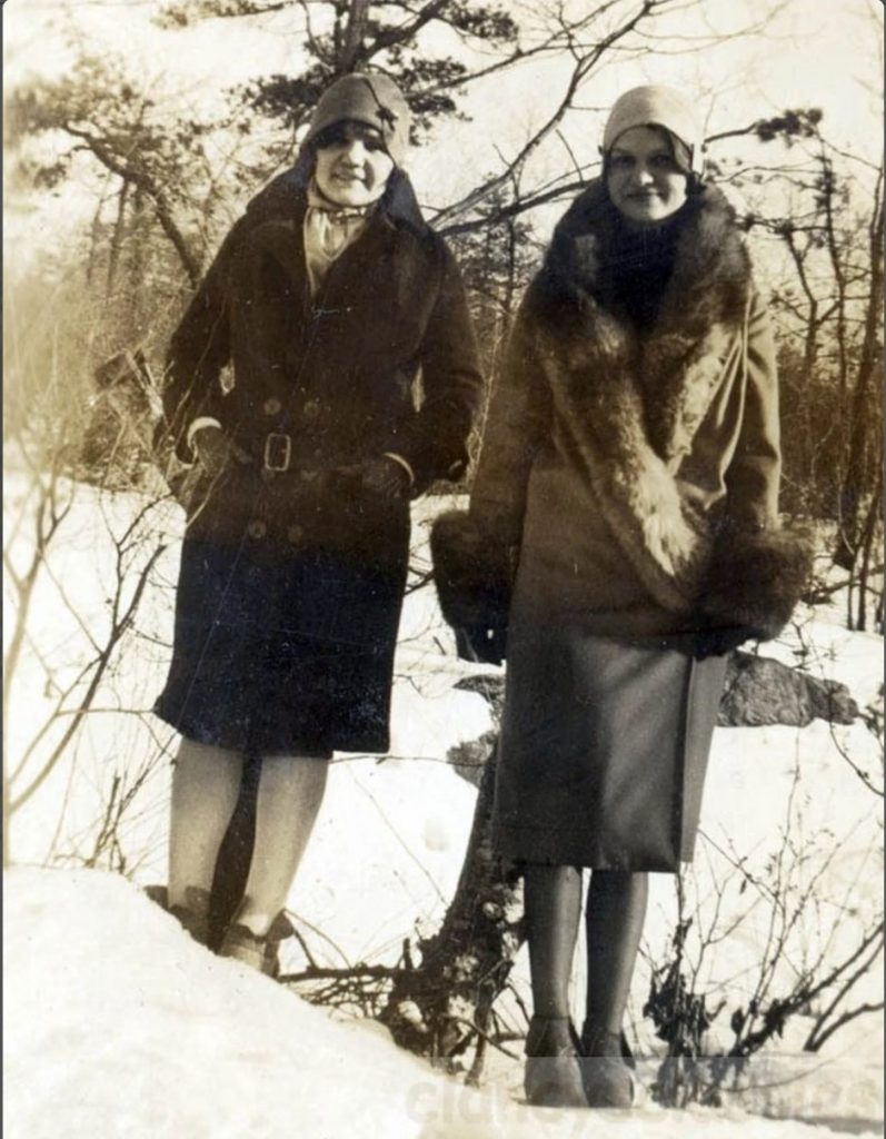 1920s vintage photo of two women in 1920s winter fashions / winter coats and cloche hats posing outside in the snow