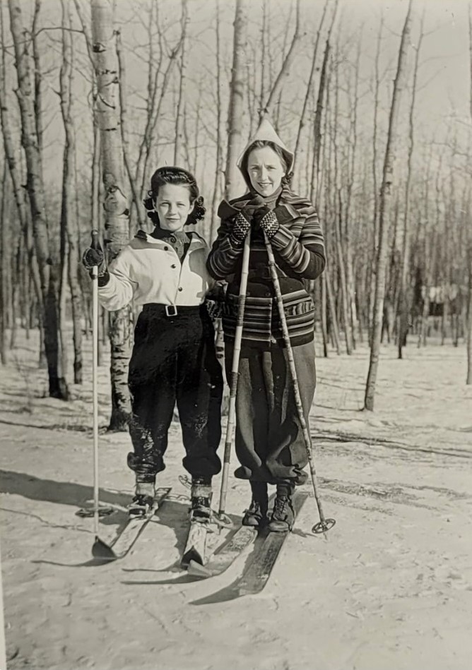 1940s vintage photo of two young women cross country skiing during the winter time in 1940s ski suits and 1940s winter hats. 