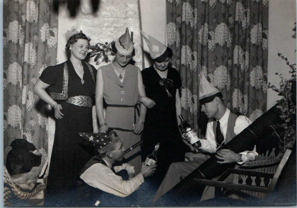 1930s vintage photo of men and women celebrating New Year's Eve in 1930s fashions, NYE Party hats and drinks.