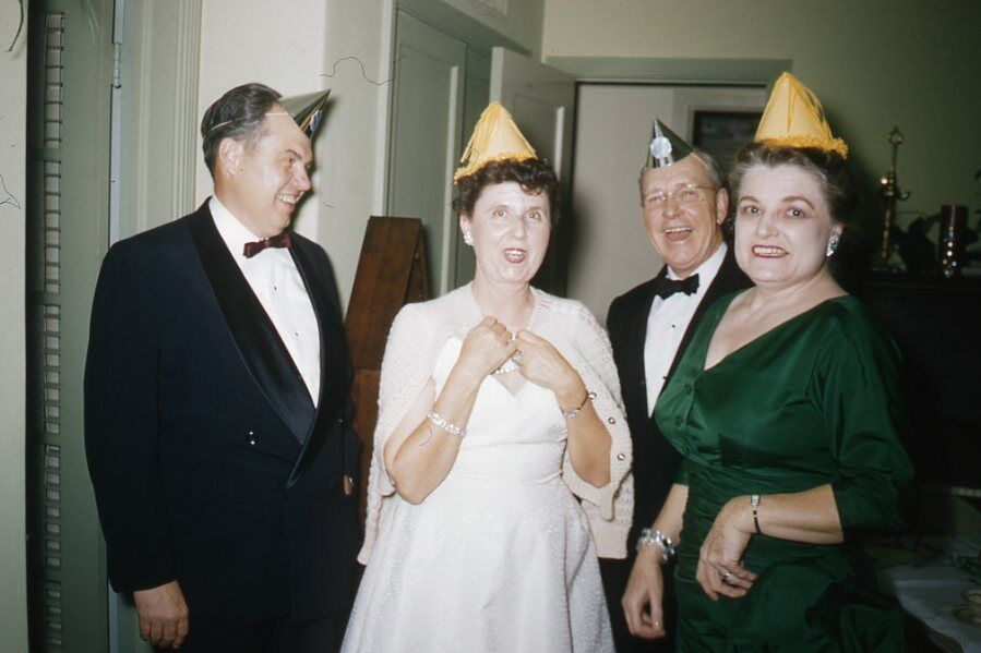 1950s vintage photo of an elegant 1950s New Year's Eve Party. The women are in evening gowns and the men in tuxedos wearing party hats. 