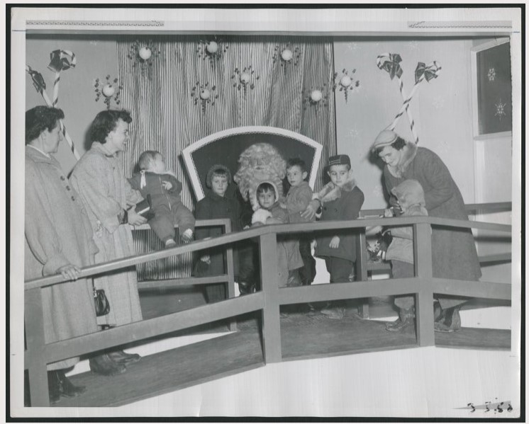 1950s vintage photo of a mall santa with men women and kids in 1950s fashions taking photos with him-1952