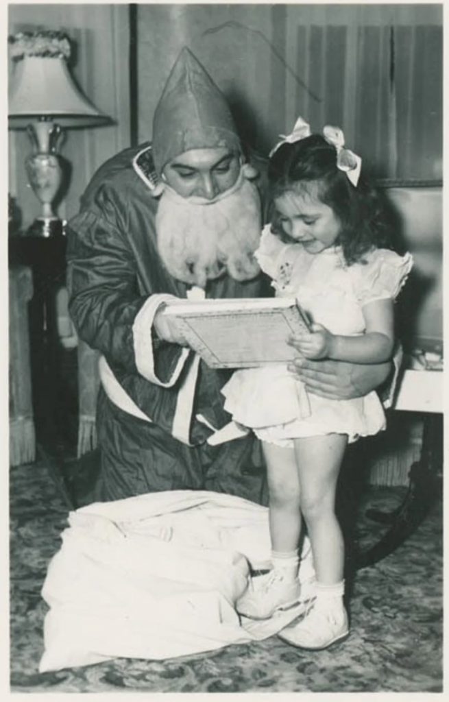 1950s vintage photo of a man dressed up as Santa Claus delivering gifts to a little girl in her livingroom