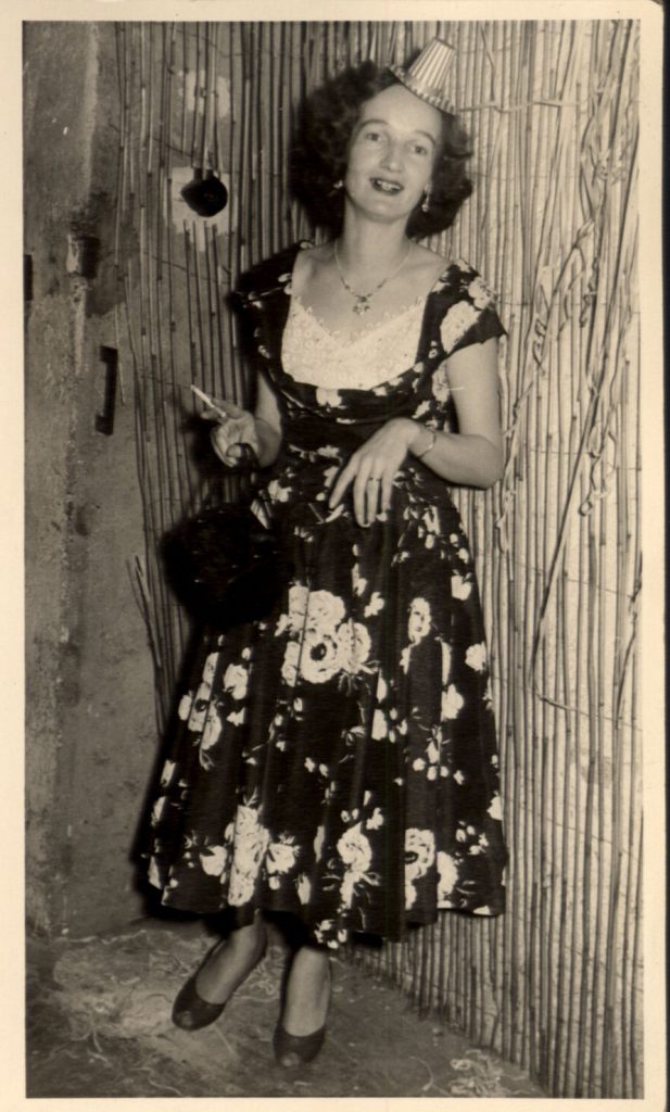 1950s vintage photo of a woman at party (possibly New Years Eve) wearing a party hat and a pretty floral 1950s dress