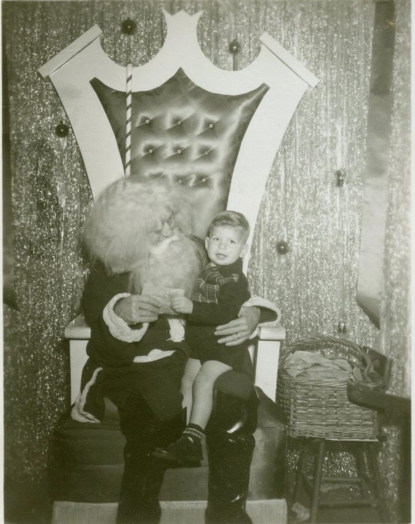 1950s vintage photo of a young boy on the lap of santa claus who has very bushy hair. 