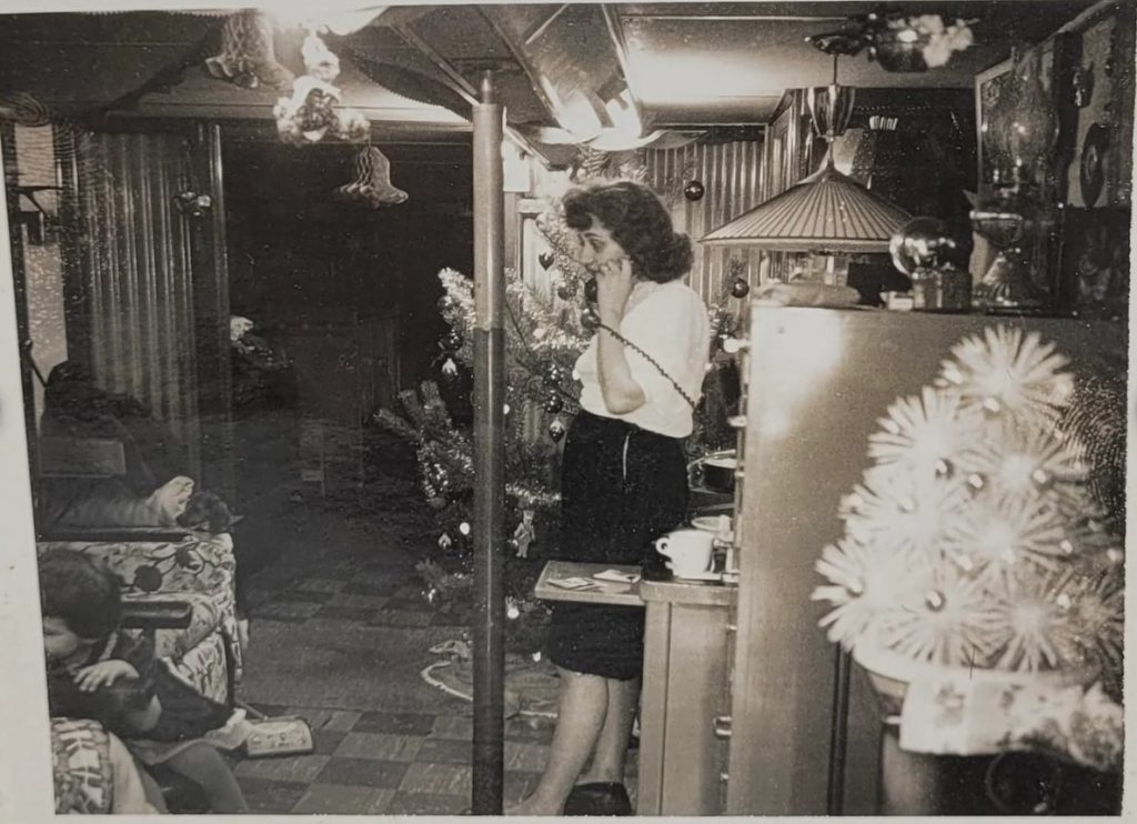  Fun  1950s/1960s photo of a woman on the phone surrounded by Christmas decorations while her kid plays on the ground. 